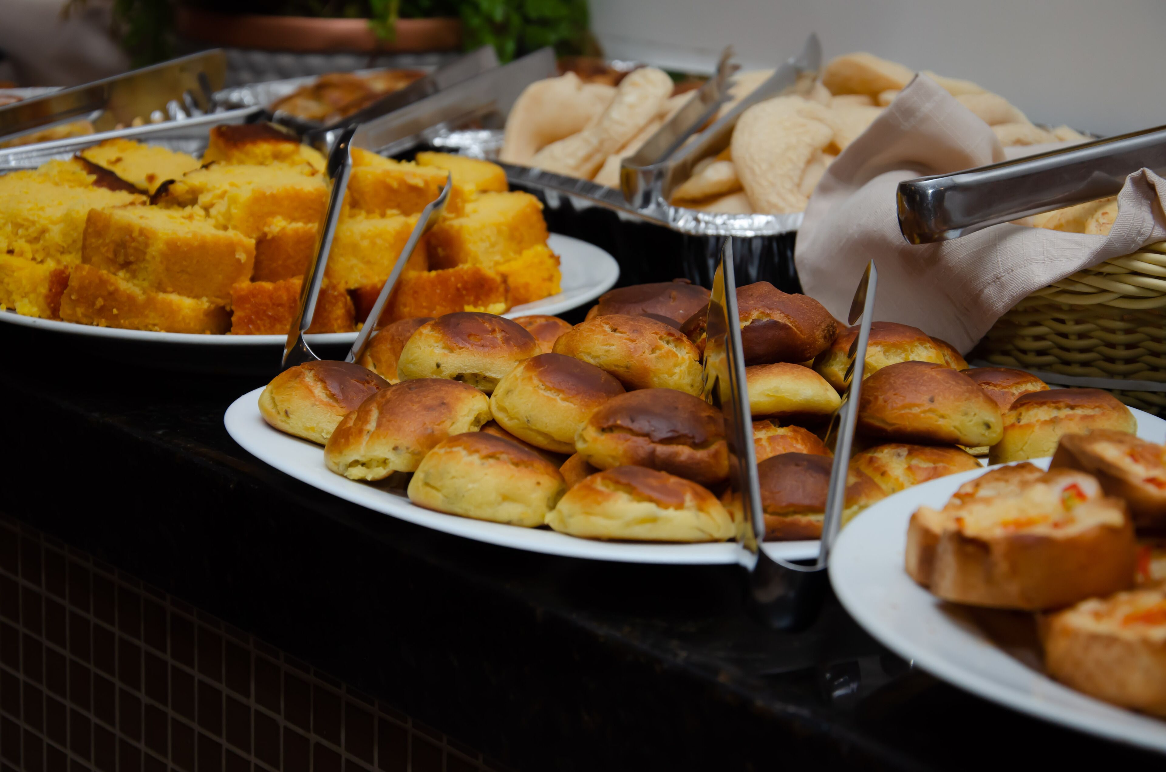 A buffet with various food items including bread rolls and cornmeal cakes.