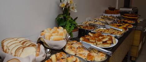 A buffet with various food items including bread, pastries, and a flower arrangement.
