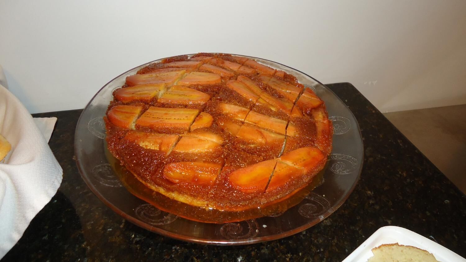 A round cake with a caramelized top, placed on a glass plate on a kitchen counter.