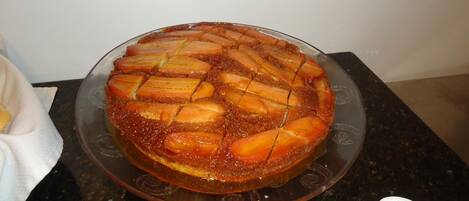 A round cake with a caramelized top, placed on a glass plate on a kitchen counter.