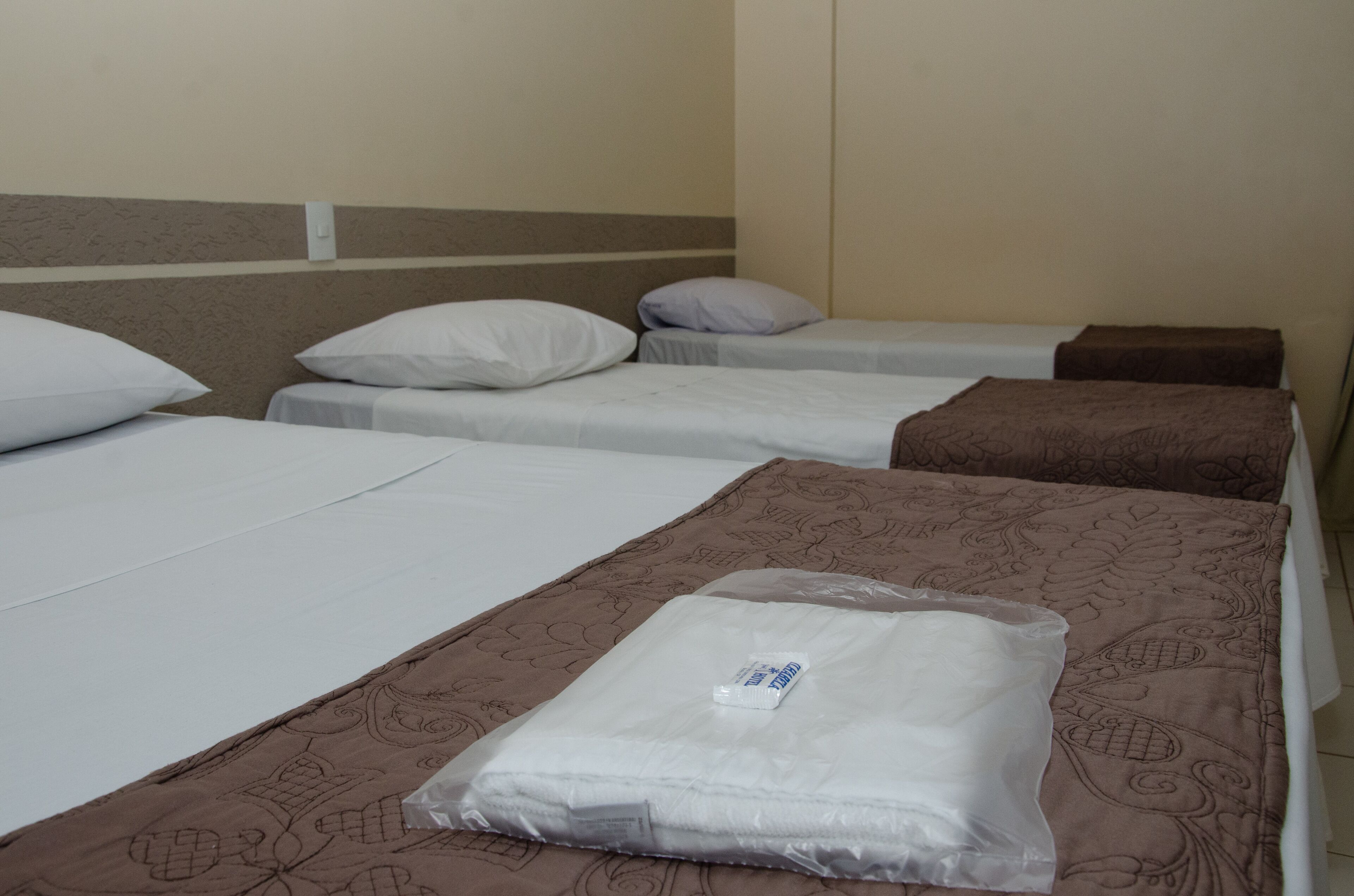 Une chambre d’hôtel avec trois lits simples, chacun étant équipé d’un oreiller et d’une couverture.