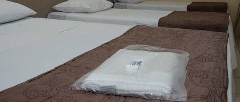 Une chambre d’hôtel avec trois lits simples, chacun étant équipé d’un oreiller et d’une couverture.