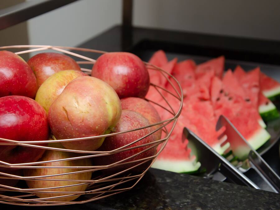 A basket of apples and watermelon slices on a countertop.