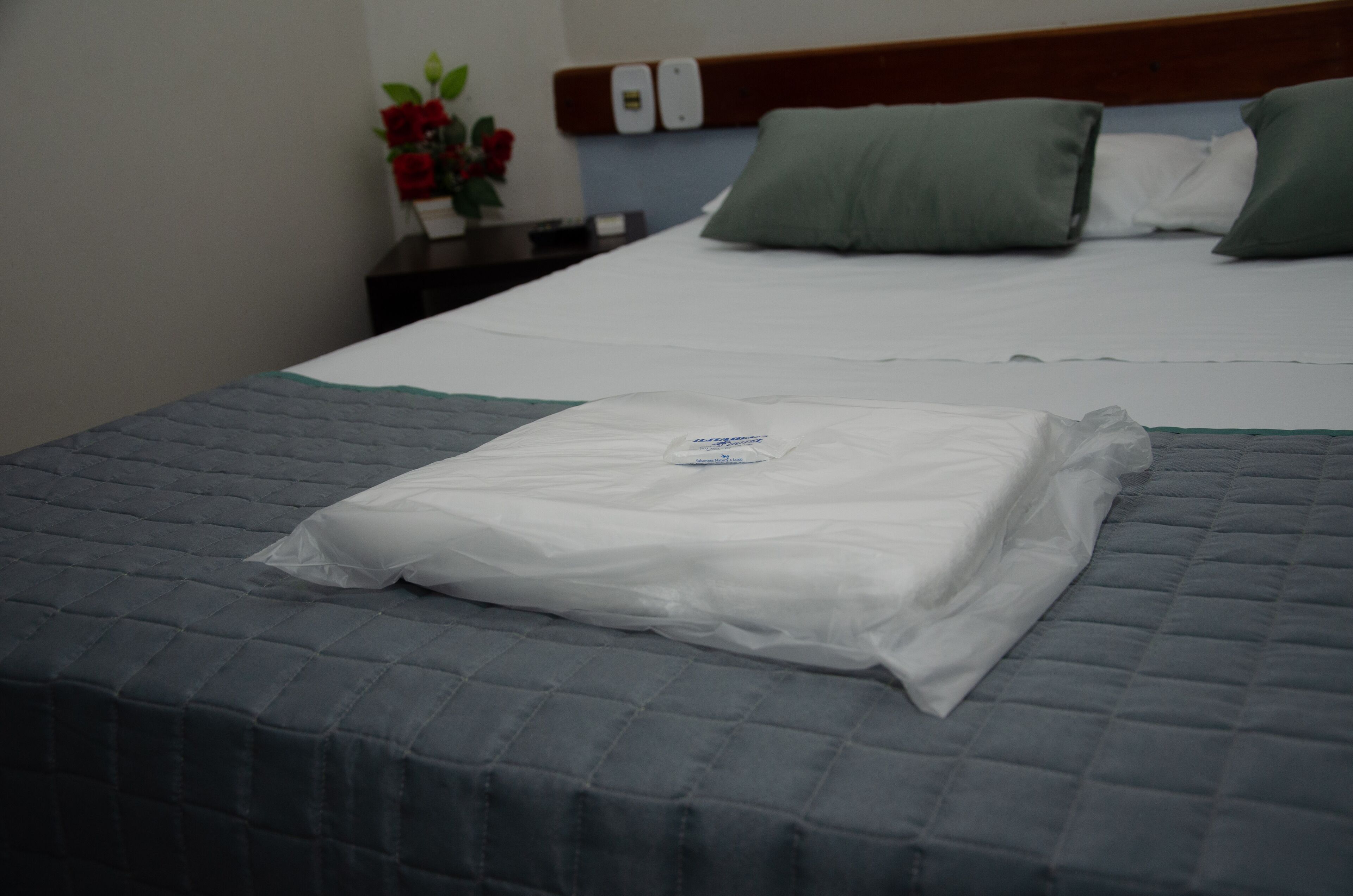 A neatly made bed with a grey quilt, a white pillow, and a green pillow on a wooden headboard.