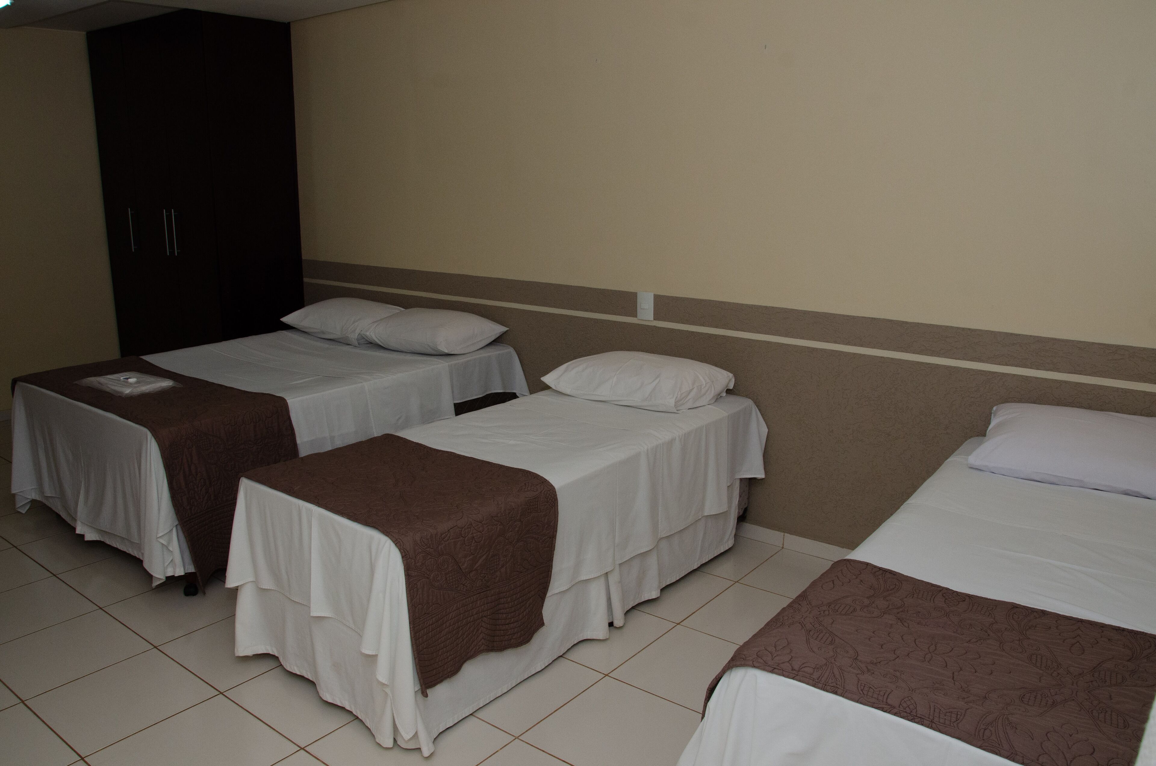 A hotel room with two single beds, a wardrobe, and a tiled floor.