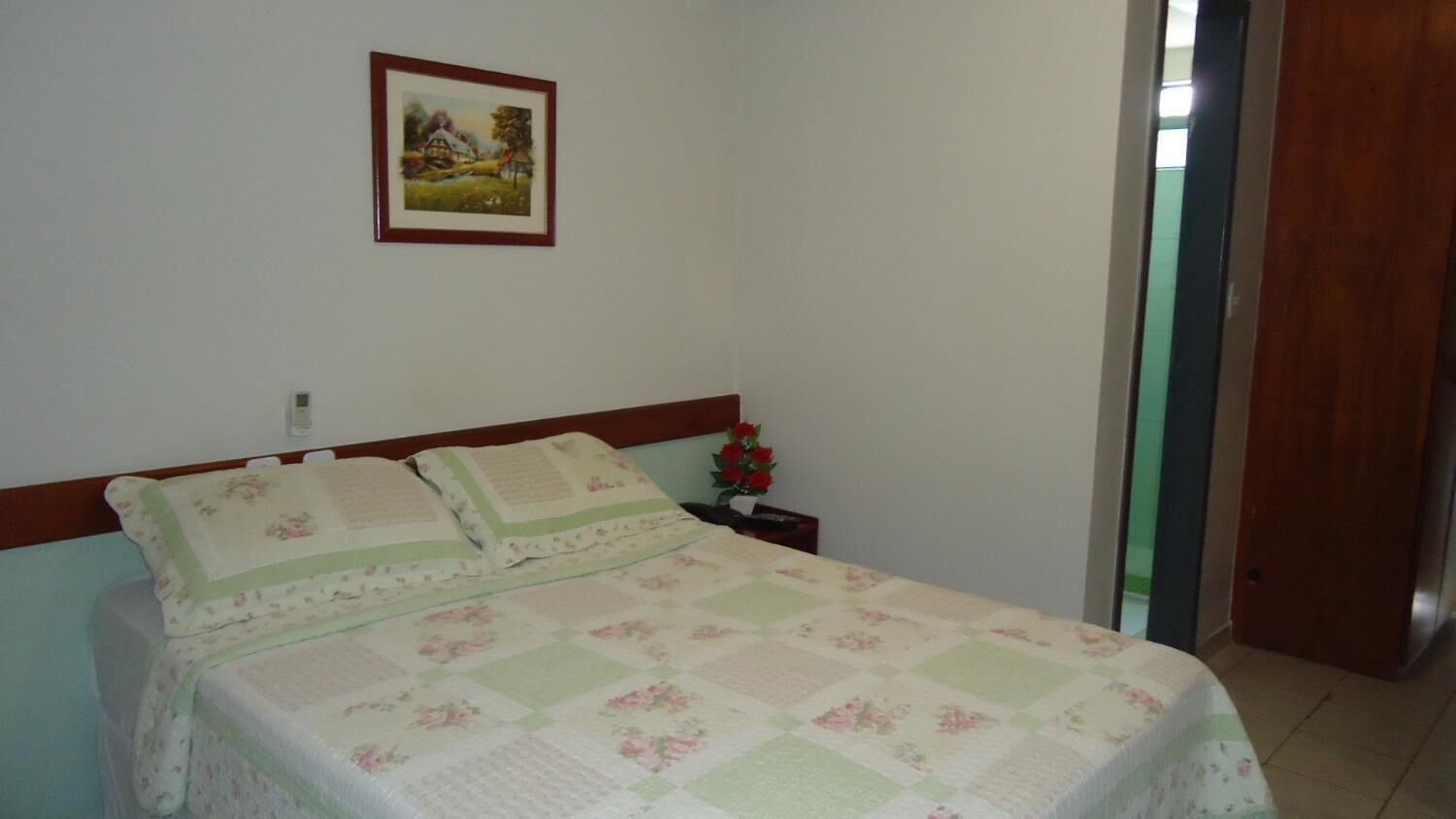 Une chambre à coucher avec un lit, une table de chevet, un tableau encadré au mur et une porte sur le côté droit.