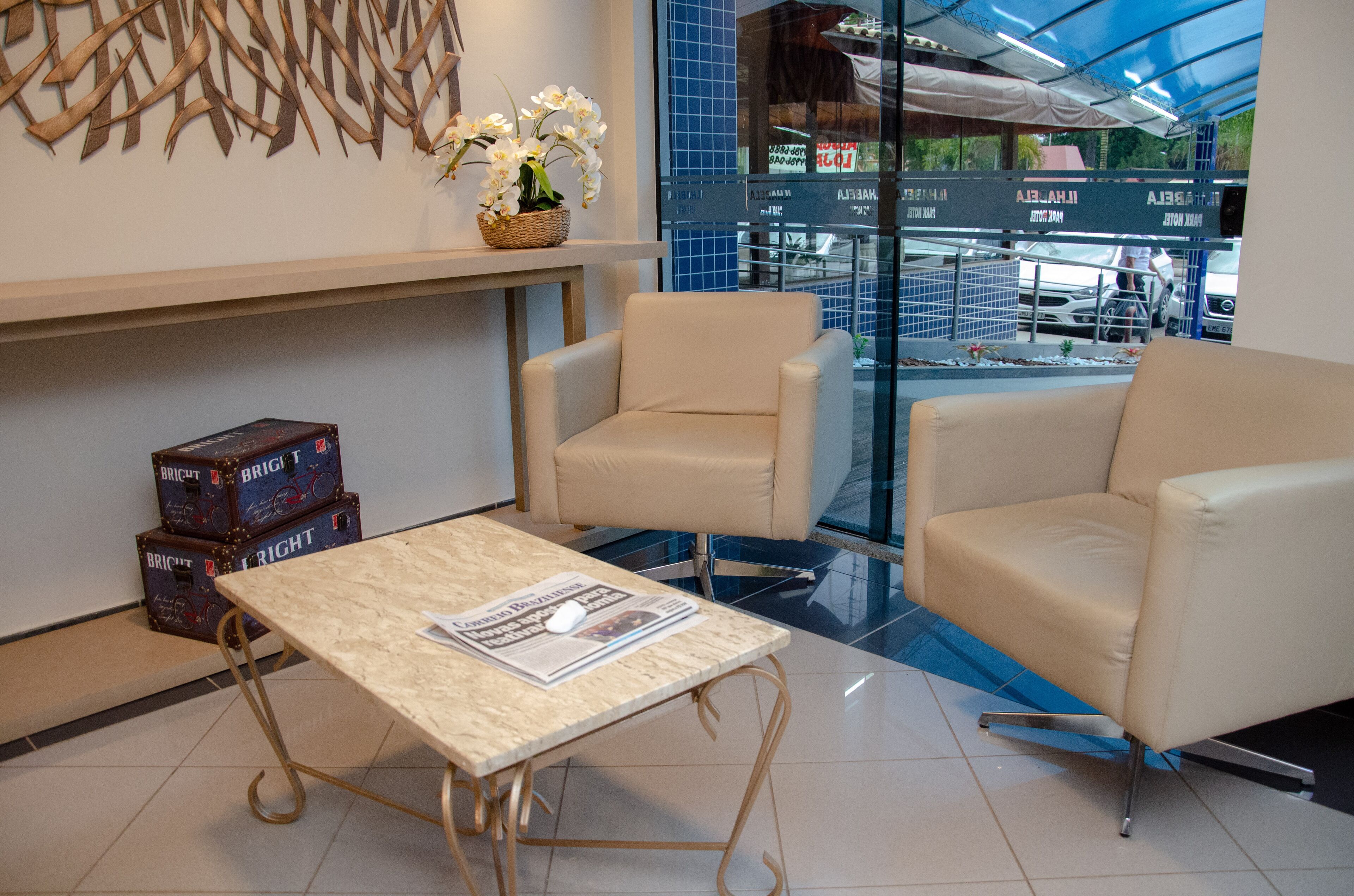 A modern hotel lobby with a marble table, leather chairs, and a view of the street through large windows.