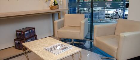 A modern hotel lobby with a marble table, leather chairs, and a view of the street through large windows.