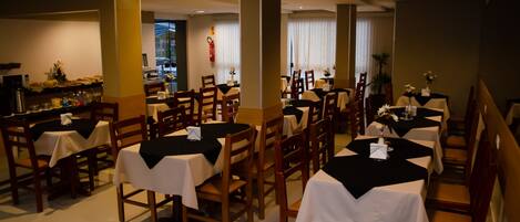 A restaurant with multiple tables and chairs, some with black tablecloths.