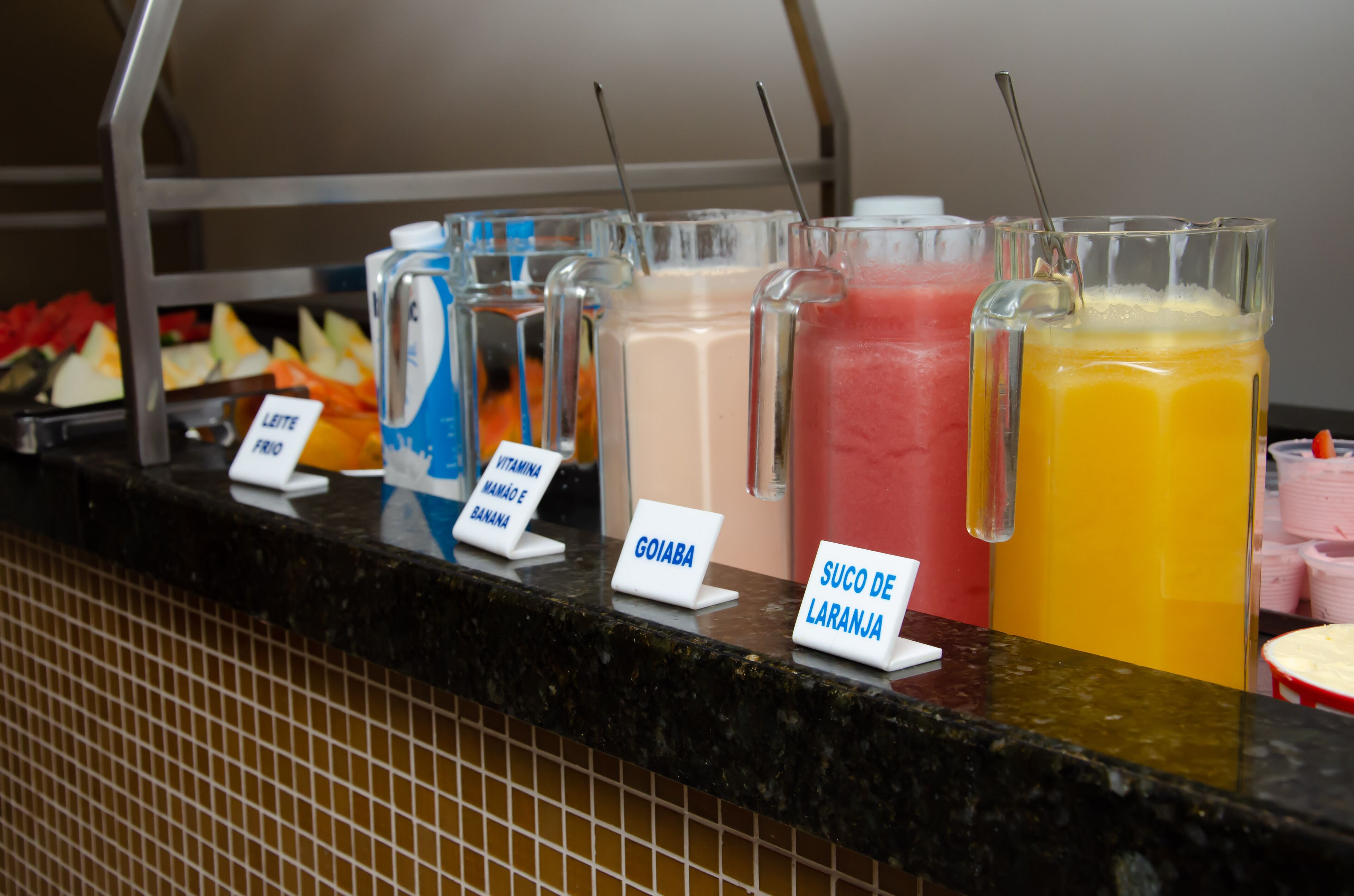 A beverage station with labeled drinks including GoIABA, SUCO DE LARANJA, and others.