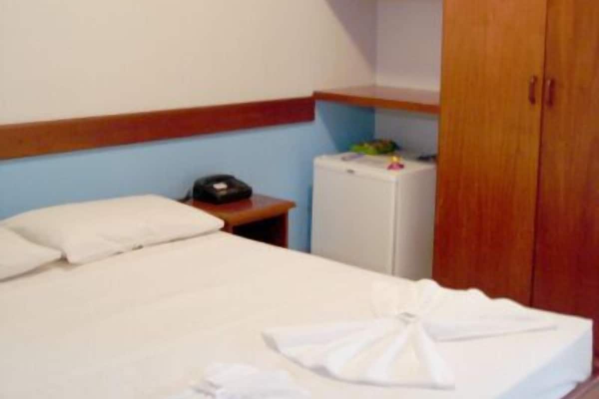 A hotel room with a bed, a bedside table with a telephone, and a small refrigerator.