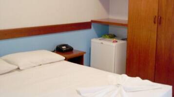 Una habitación de hotel con una cama, una mesita de noche con teléfono y un refrigerador pequeño.