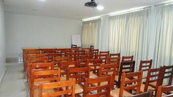 Un salón de conferencias con filas de sillas de madera, una mesa larga y un proyector en el techo.