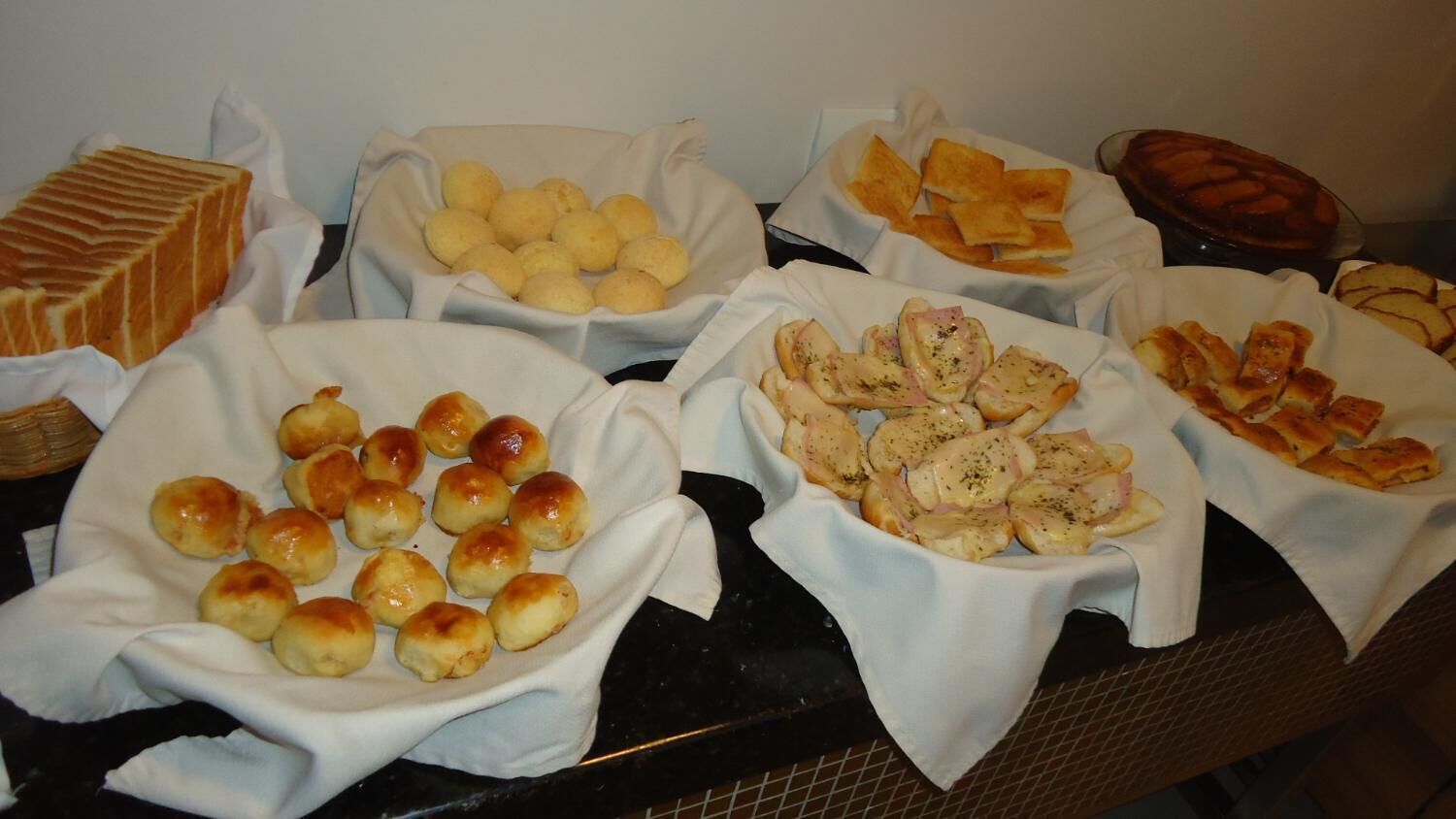 A buffet with various food items including bread rolls, cheese slices, and a dessert.