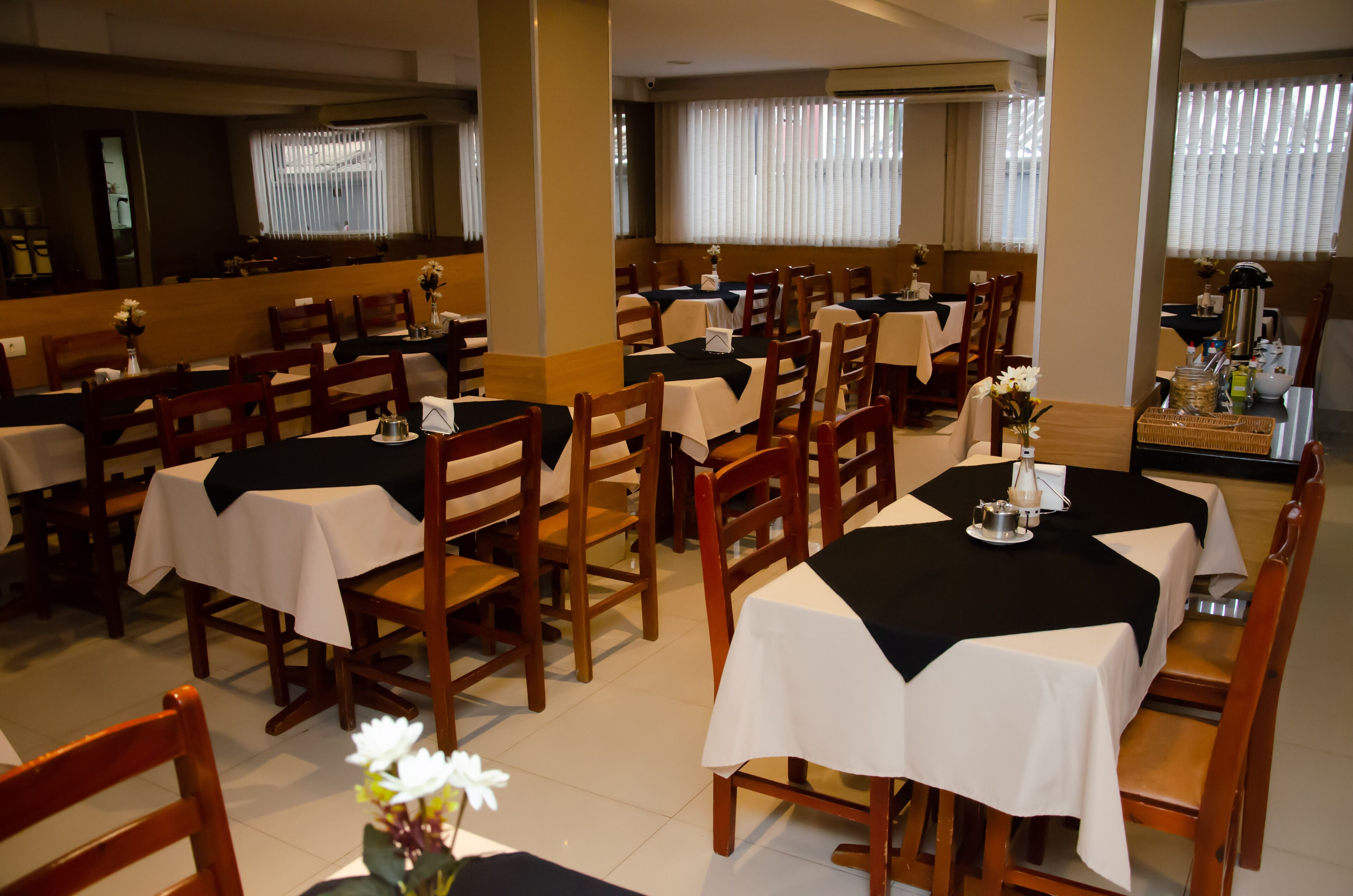 A restaurant with multiple tables and chairs, some with black tablecloths and others with white.