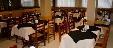 A restaurant with multiple tables and chairs, some with black tablecloths and others with white.