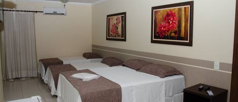 Ein Hotelzimmer mit zwei Betten, einem kleinen Nachttisch, einer Wand-Klimaanlage und zwei gerahmten Blumenbildern.