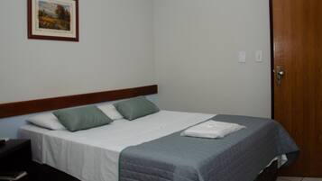 A neatly made bed with a grey quilt, two green pillows, and a white blanket folded at the foot.