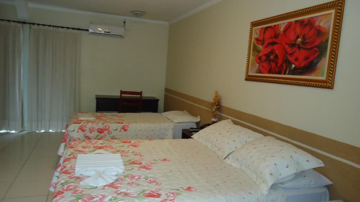 A hotel room with two beds, a chair, a desk, and a painting on the wall.