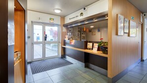 Un área de recepción con un mostrador de madera, una entrada con puerta de cristal y un letrero que dice