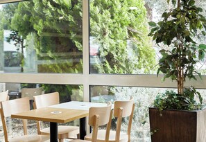 A dining area with a table and chairs, large windows, and a potted plant.