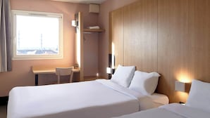 Habitación de hotel con dos camas, un escritorio y una ventana con vistas.