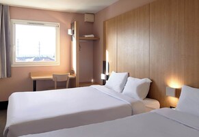 A hotel room with two beds, a desk, and a window with a view.