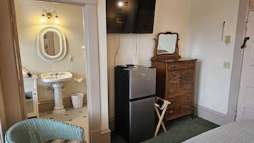 A hotel room with a bed, a dresser, a television, a refrigerator, a sink, and a wicker chair.