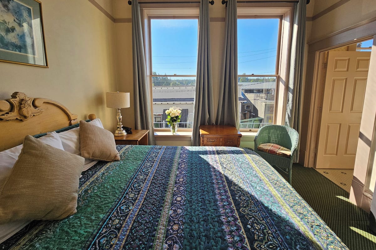 A hotel room with a large bed, a nightstand, a lamp, a chair, and a window with curtains.