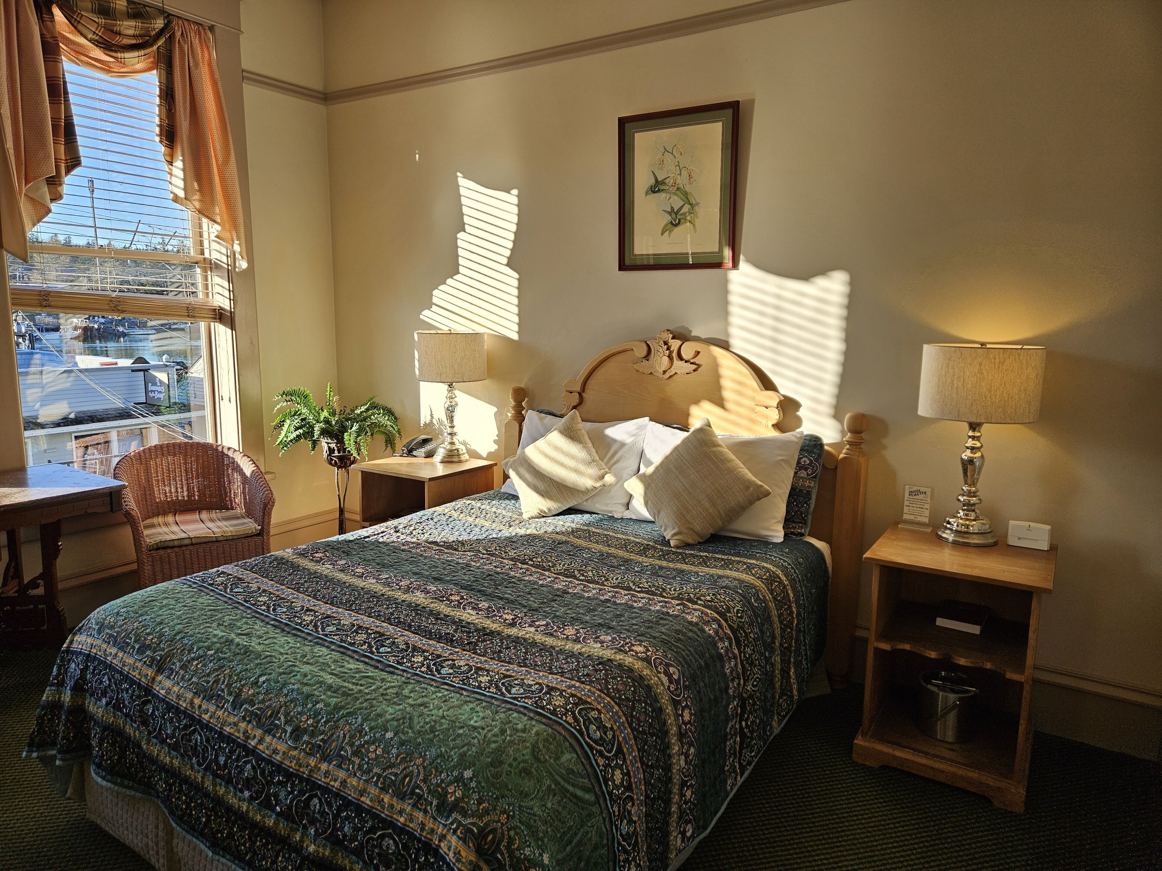 Une chambre à coucher bien rangée, avec un grand lit, deux tables de chevet, une chaise et une fenêtre avec des rideaux.