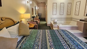 A hotel room with a large bed, a sitting area with a table and chairs, a bathroom with a bathtub and sink, and a television in the corner.
