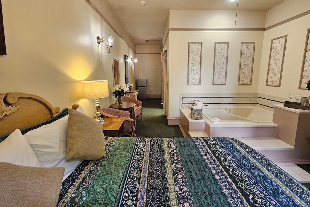 A hotel room with a large bed, a sitting area with a table and chairs, a bathroom with a bathtub and sink, and a television in the corner.