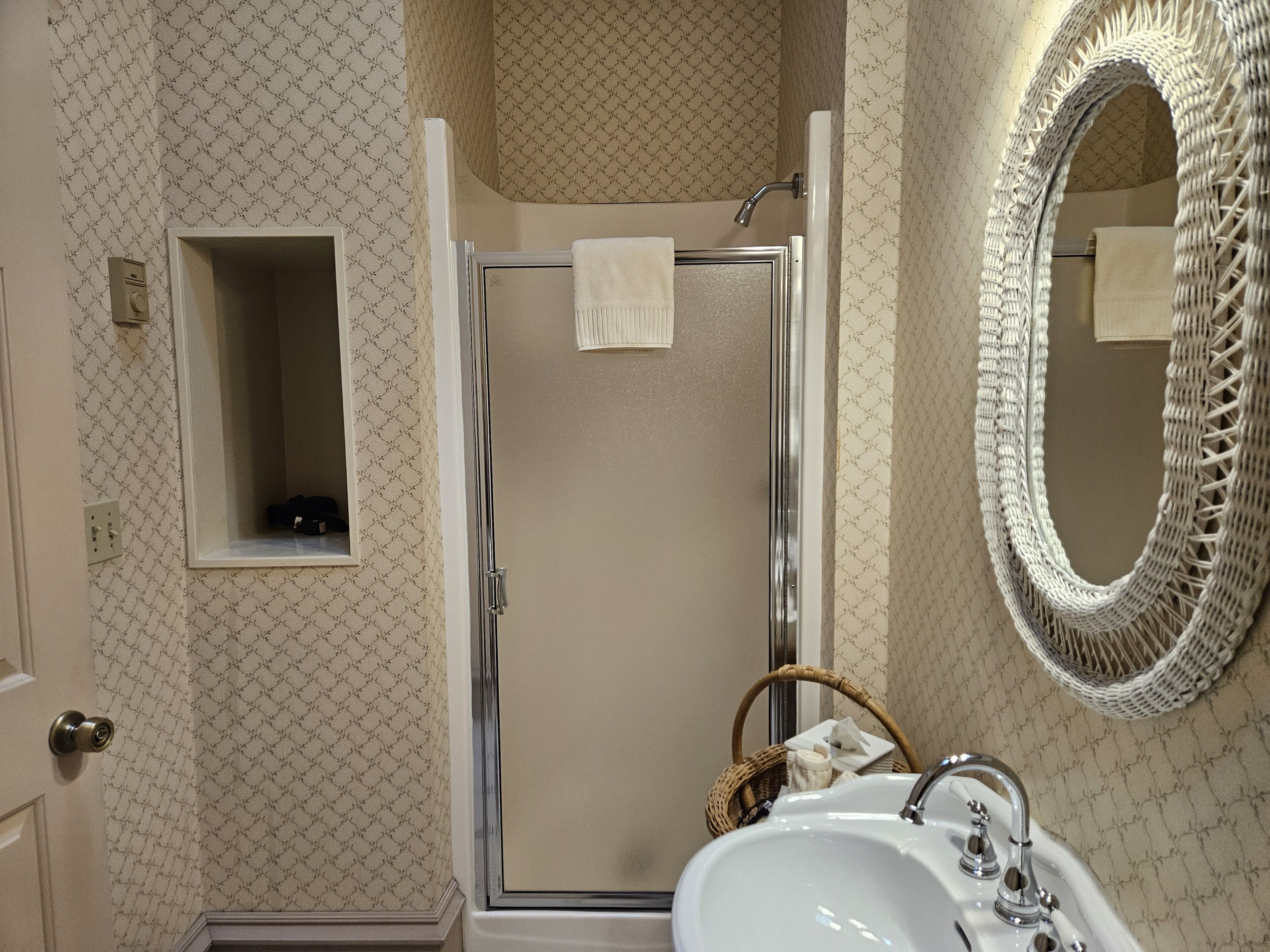 A bathroom with a glass shower enclosure, a white sink, a large mirror, and a small window.