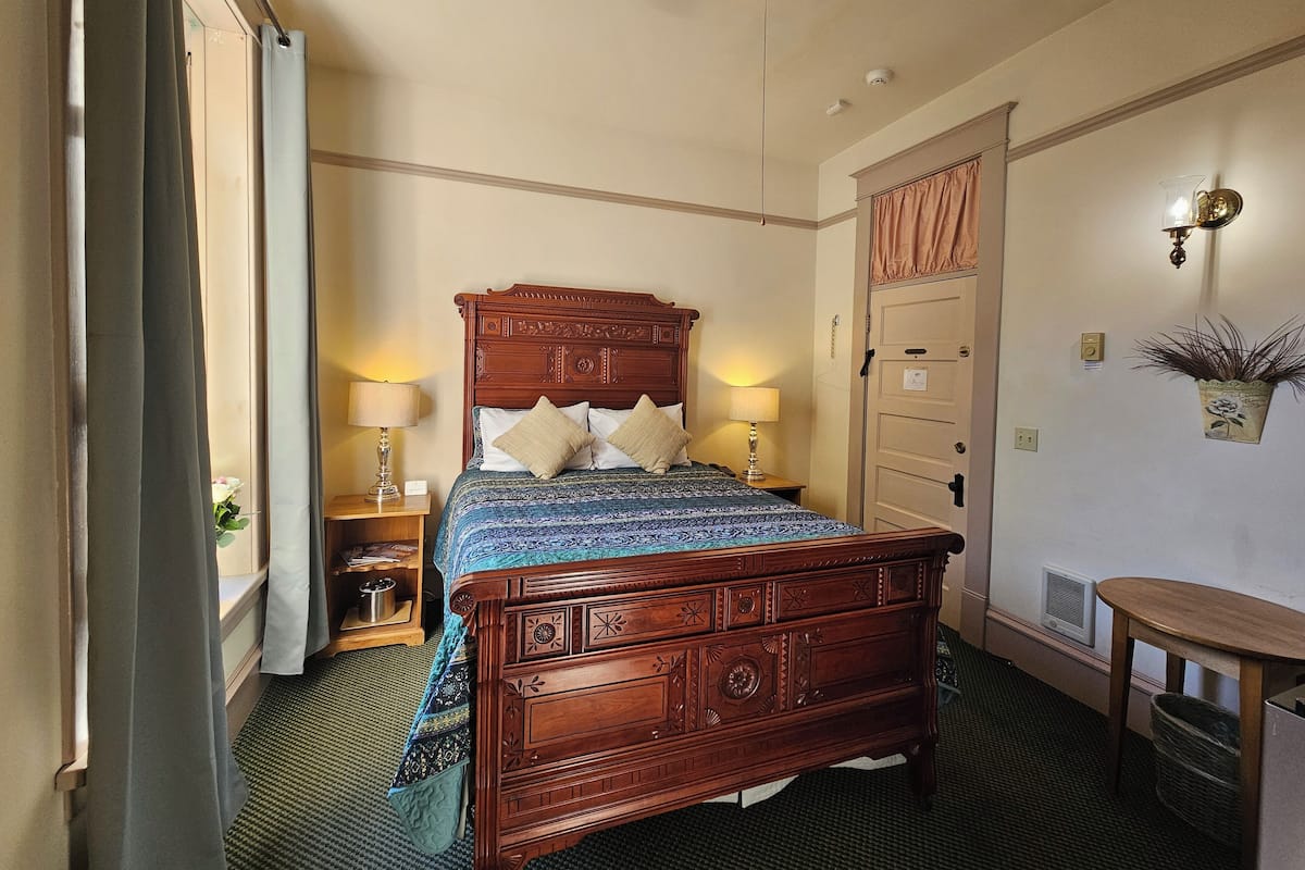 A neatly arranged bedroom with a wooden bed, two bedside tables with lamps, a small wooden table, and a potted plant on the wall.