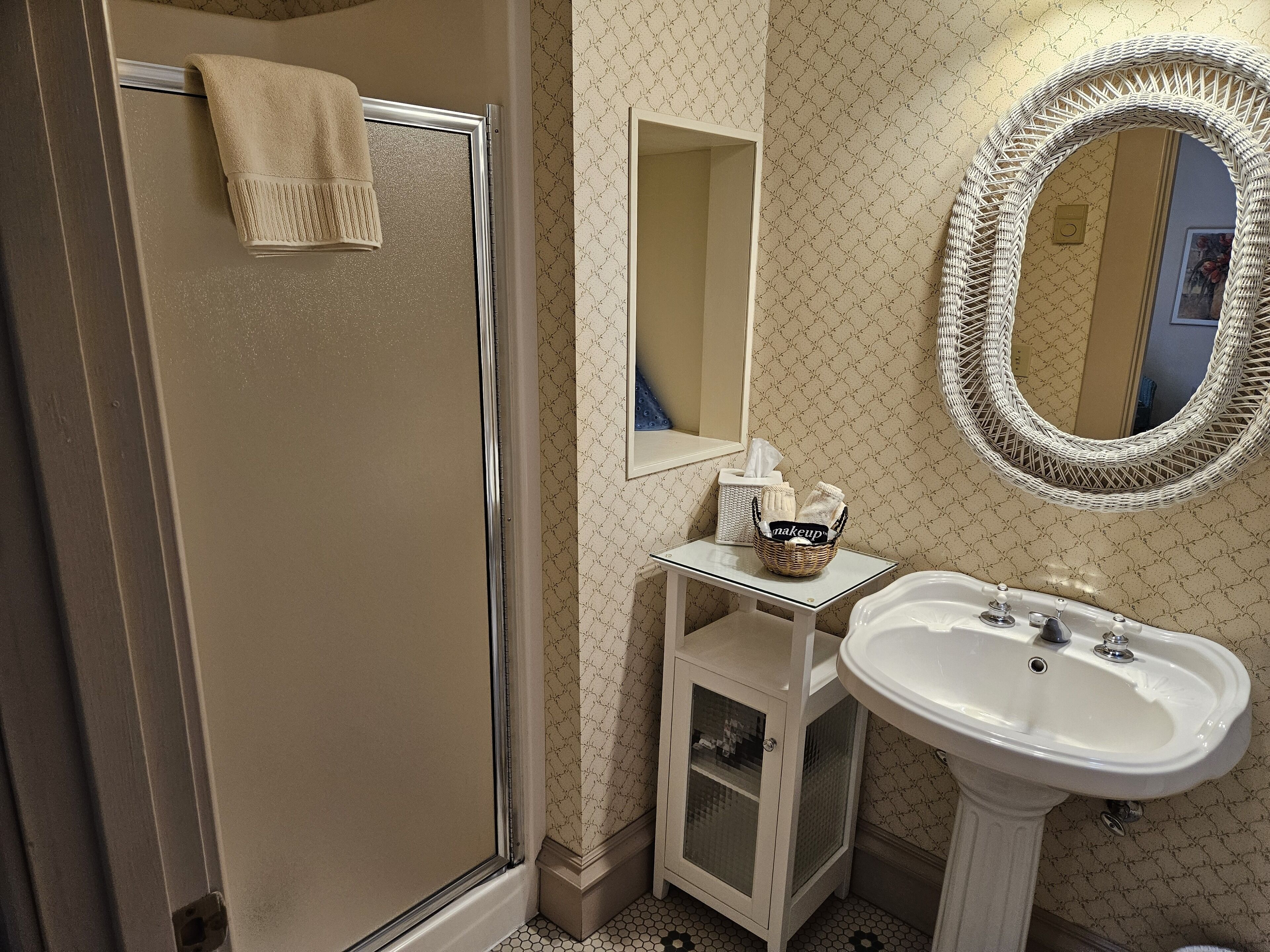 A bathroom with a shower, a sink, a mirror, and a basket with toiletries.