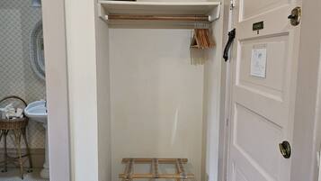 A corner room with a white door, a small shelf with a fan, a drying rack, and a patterned floor.