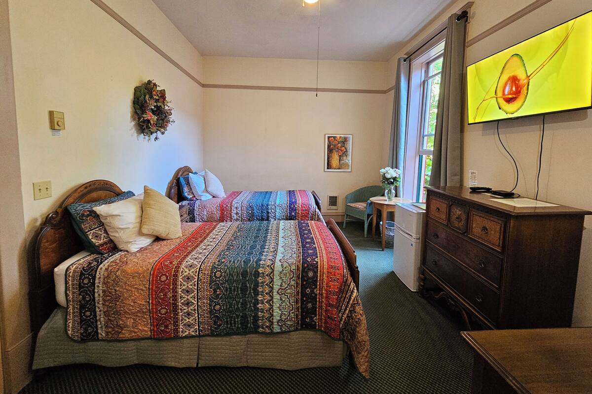 A bedroom with a bed, dresser, desk, and a television.