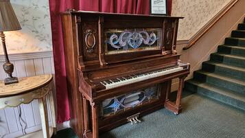 Un piano de cola en el vestíbulo de un hotel, con una escalera y un cartel enmarcado encima.