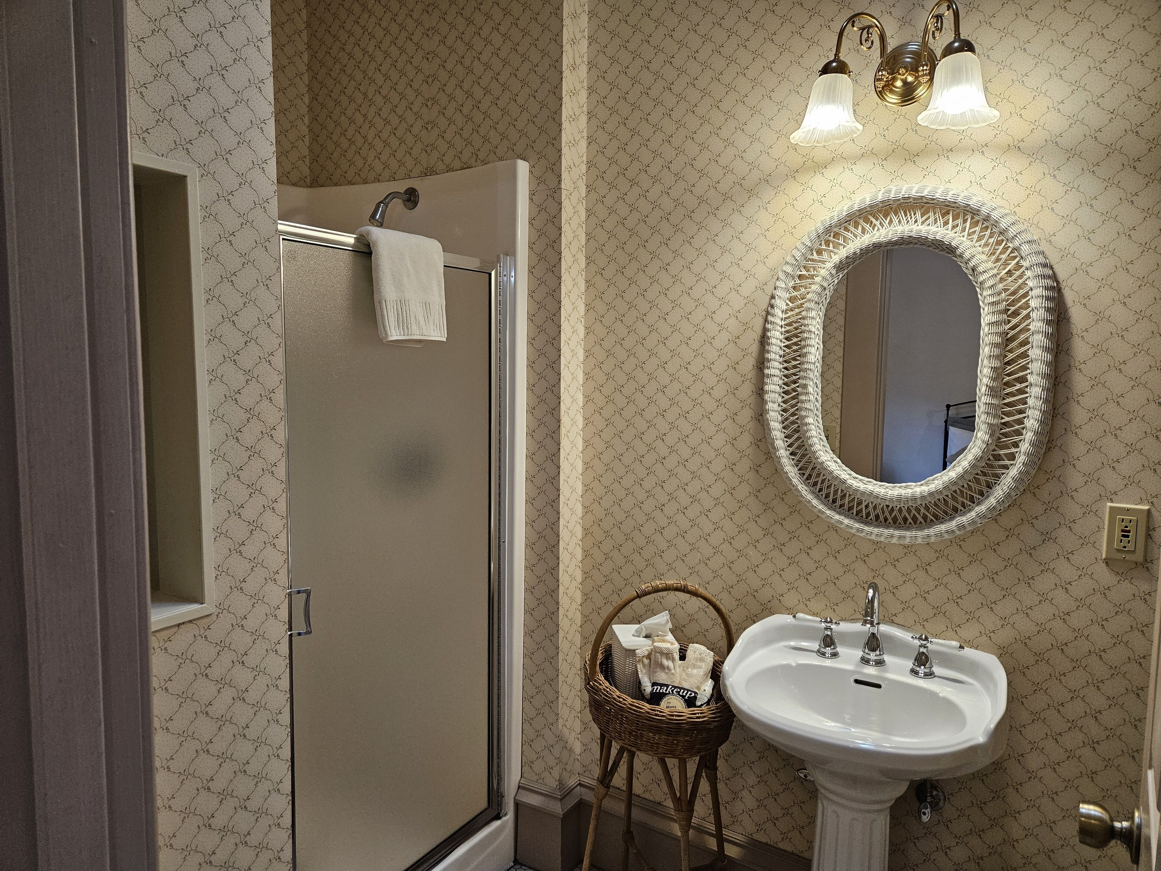 A bathroom with a shower, a sink, a mirror, and a wall-mounted light fixture.