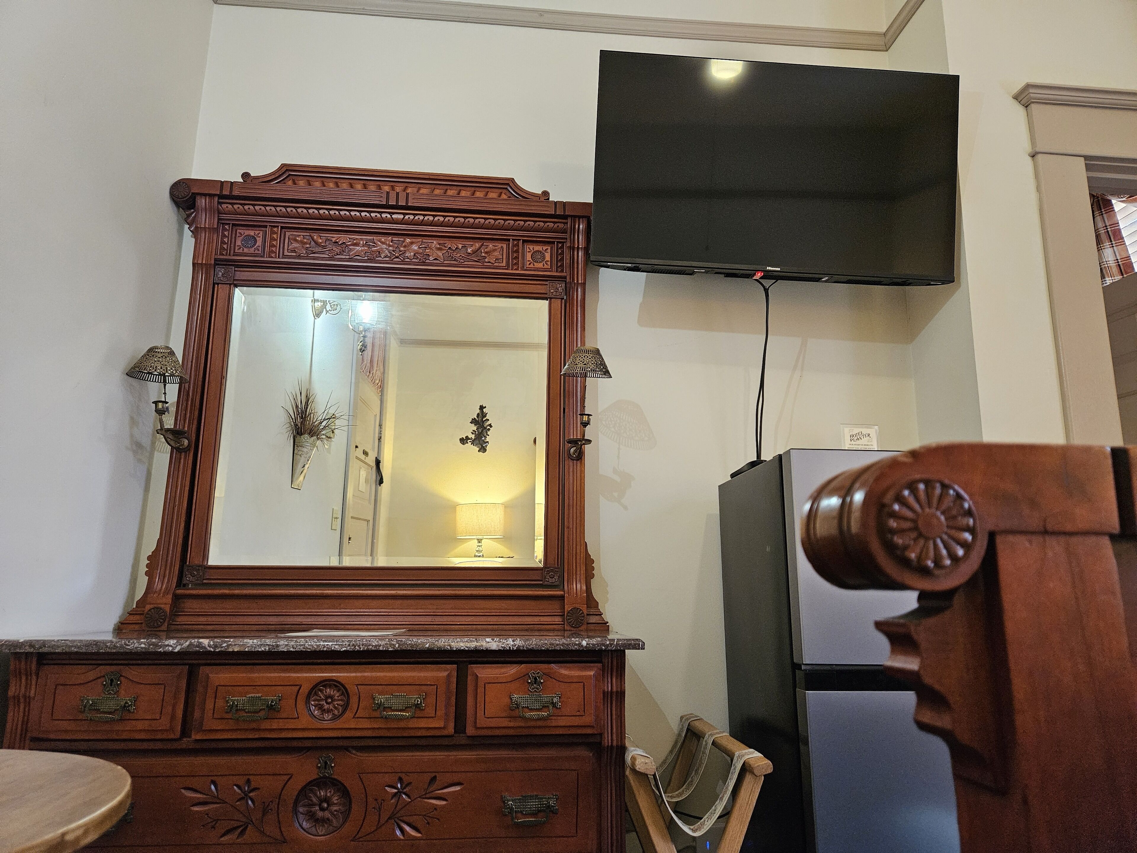 A wooden dresser with drawers and a mirror, a television mounted on the wall, and a refrigerator.