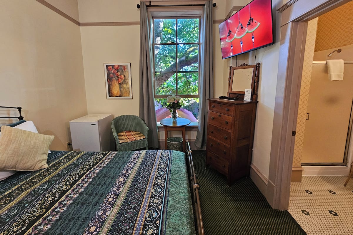 A bedroom with a bed, dresser, chair, and a television on the wall.