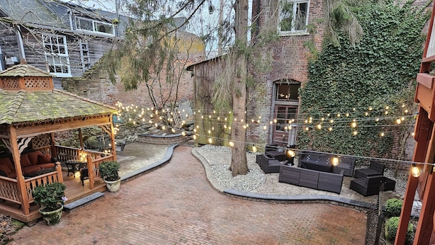 A courtyard with a wooden gazebo, outdoor seating, and string lights.