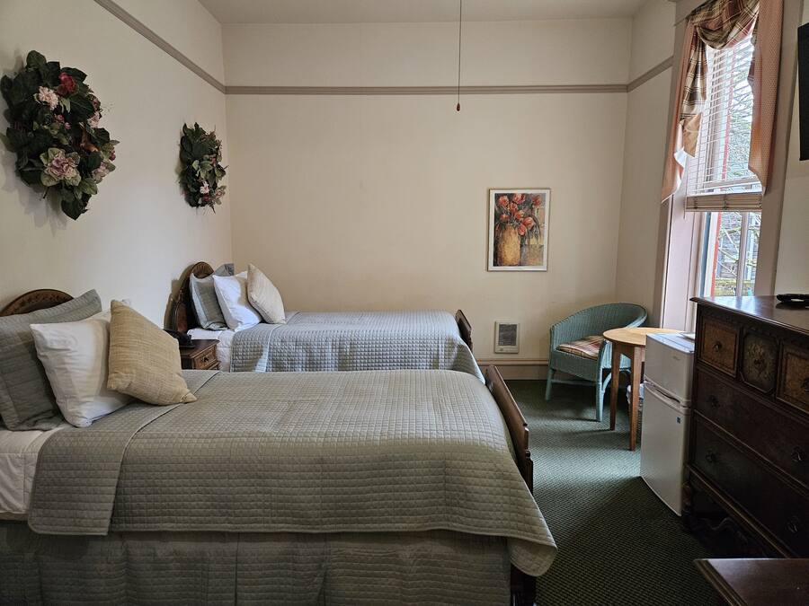 A bedroom with two beds, a dresser, a chair, a painting, and a window with curtains.