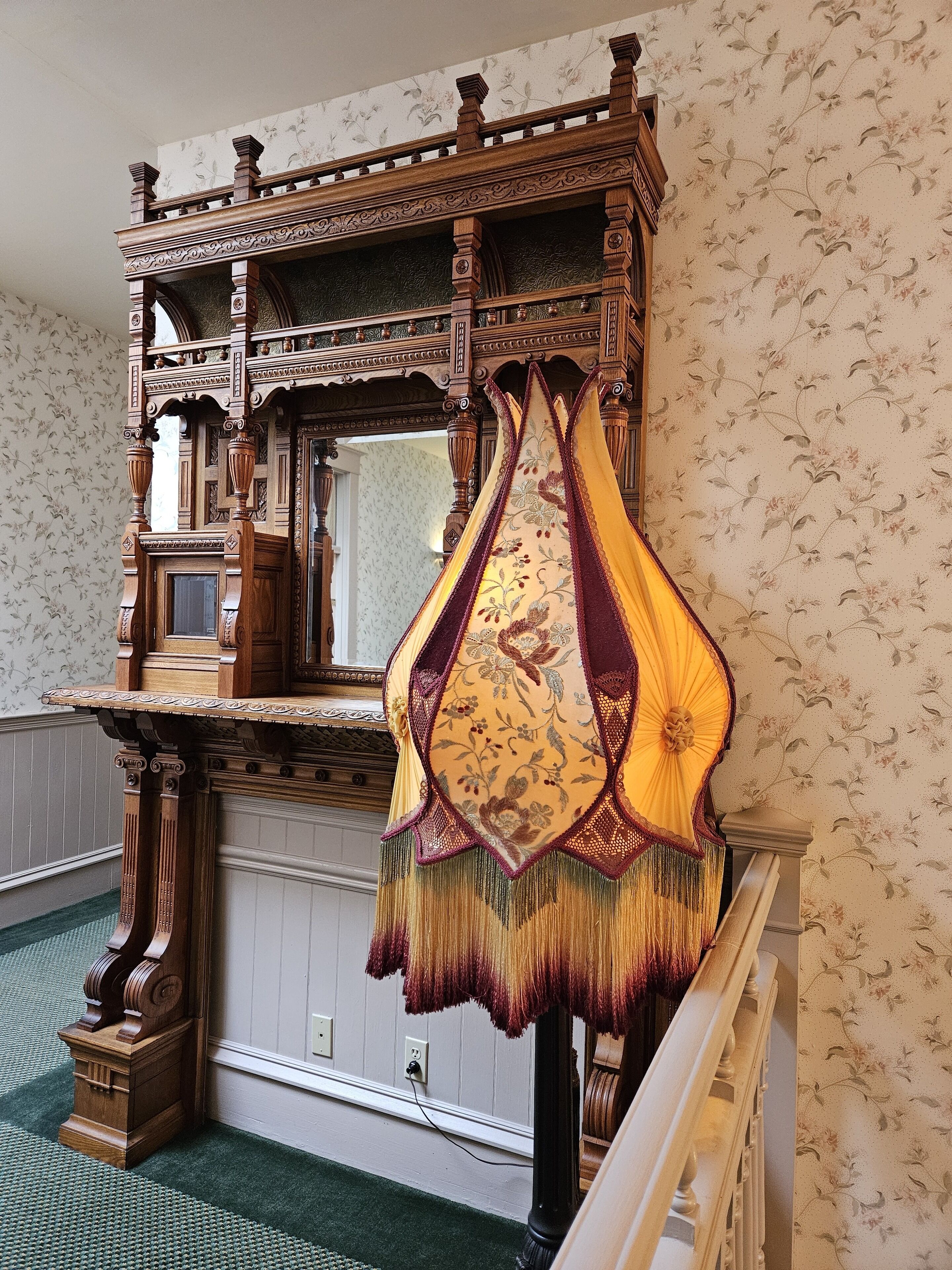 A room with a wooden staircase, a patterned wallpaper, and a decorative hanging.