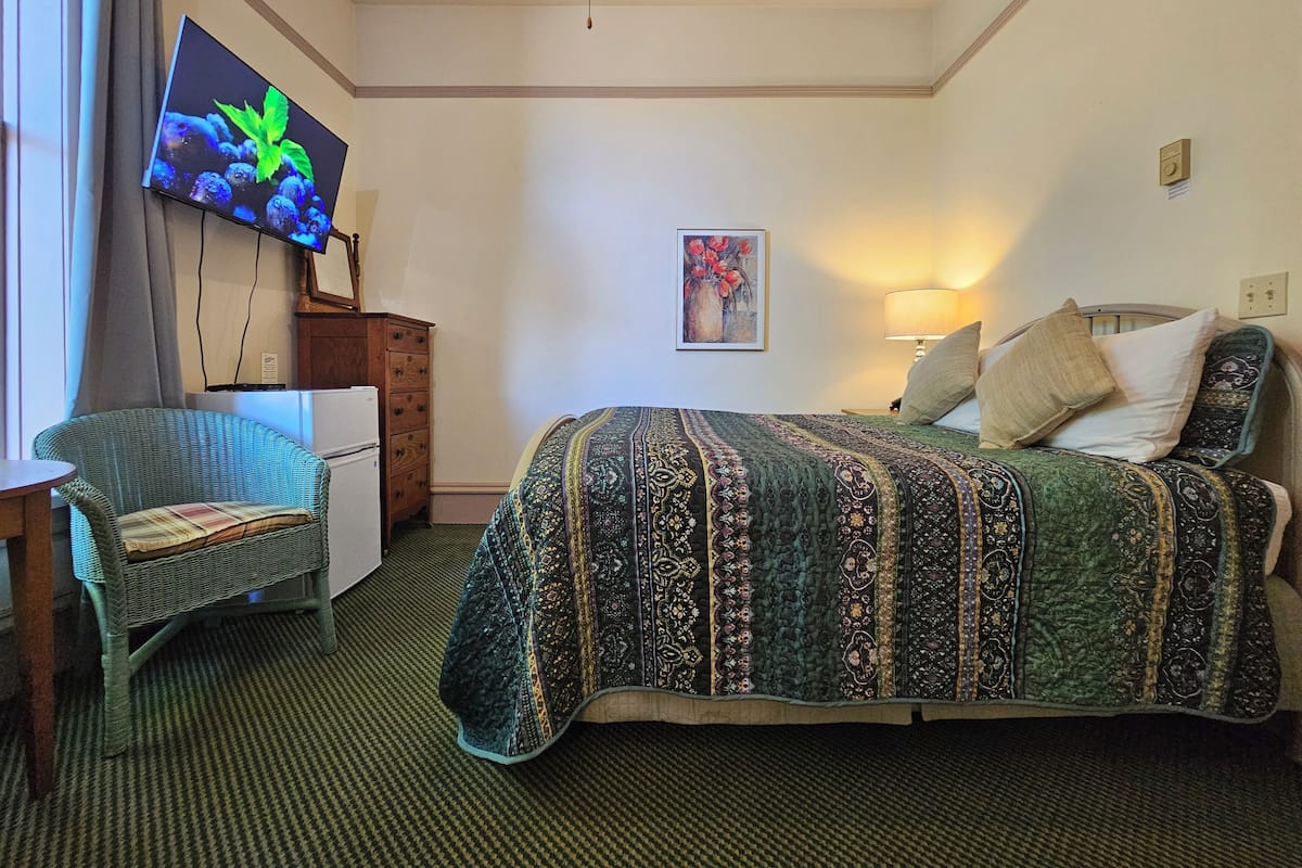A hotel room with a bed, a chair, a television, a painting, and a lamp.
