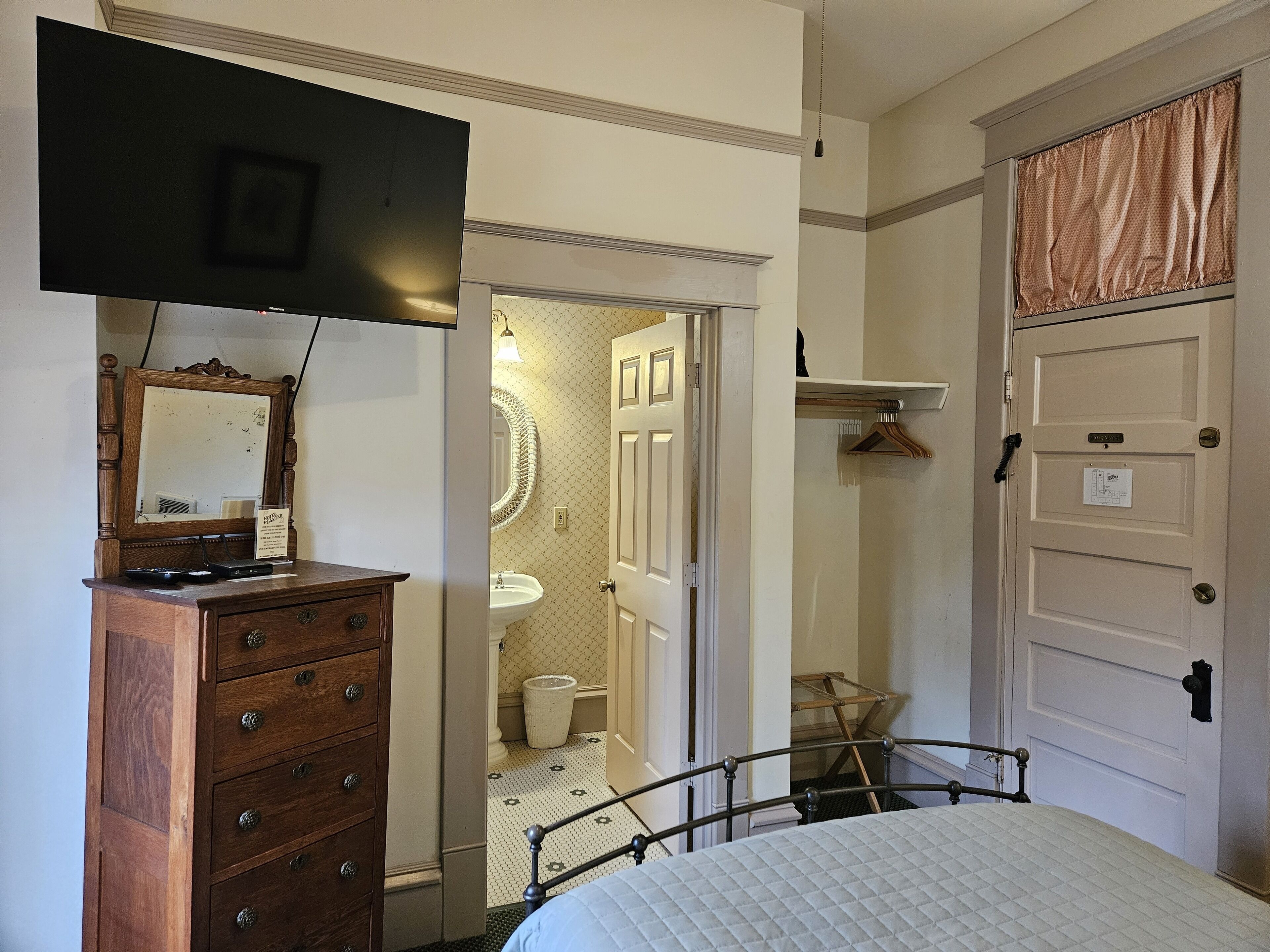 A bedroom with a bed, dresser, television, and a bathroom visible through an open door.