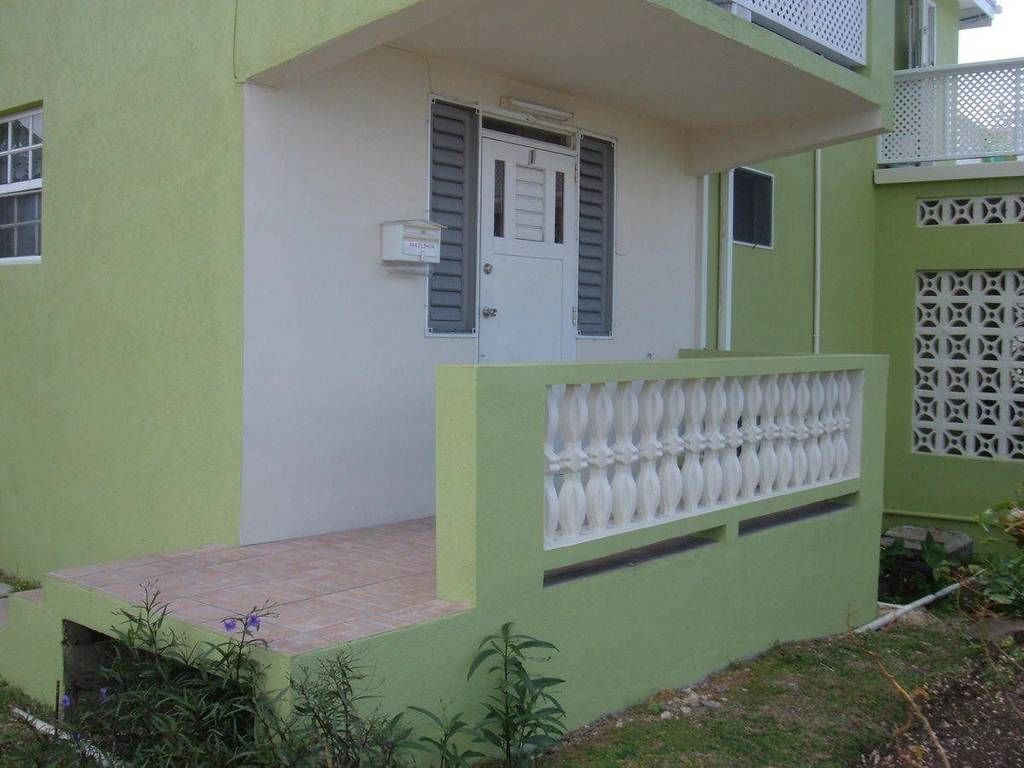 Un edificio con fachada verde, una puerta blanca con contraventanas y un pequeño porche.