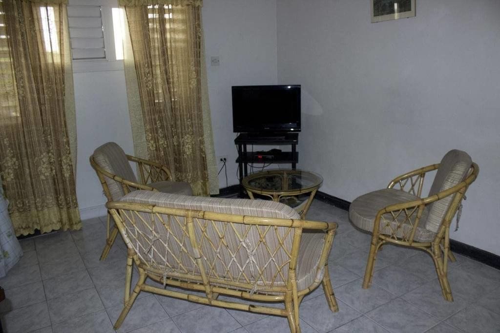 A living room with a television, two wicker chairs, a glass coffee table, and curtains.