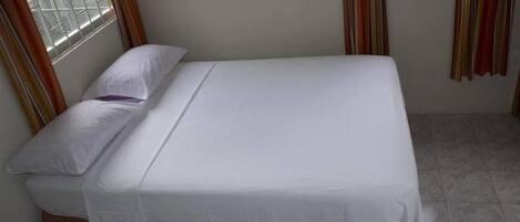 Una cama individual con ropa de cama blanca en una habitación con ventana y cortinas.