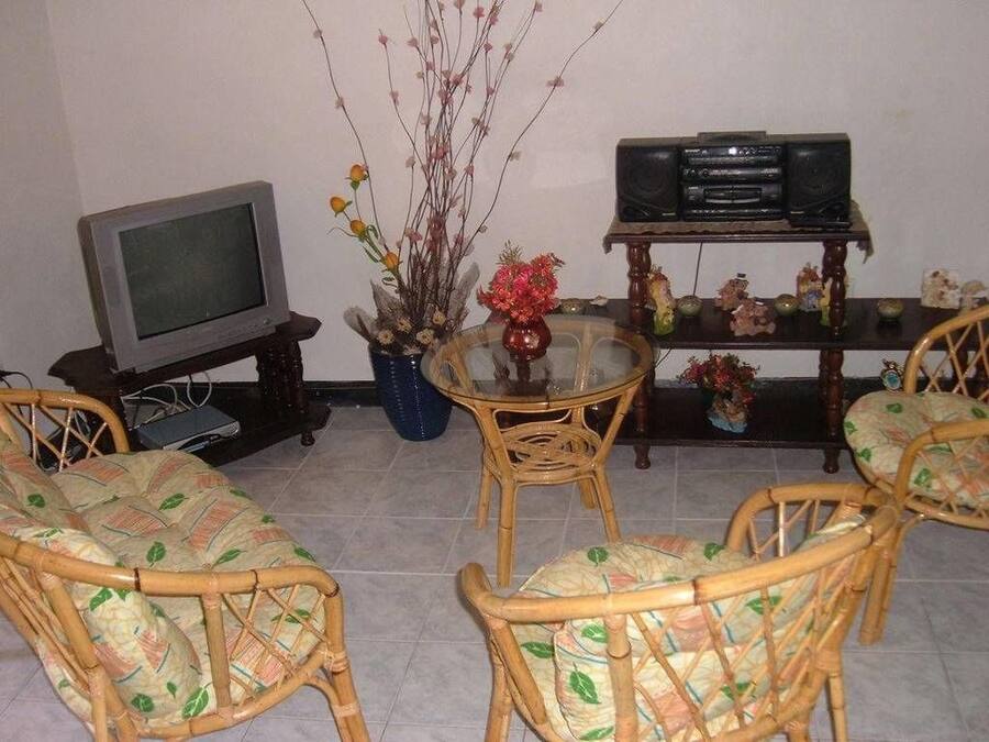 A living room with a television, a small table with chairs, and a shelf with decorative items.
